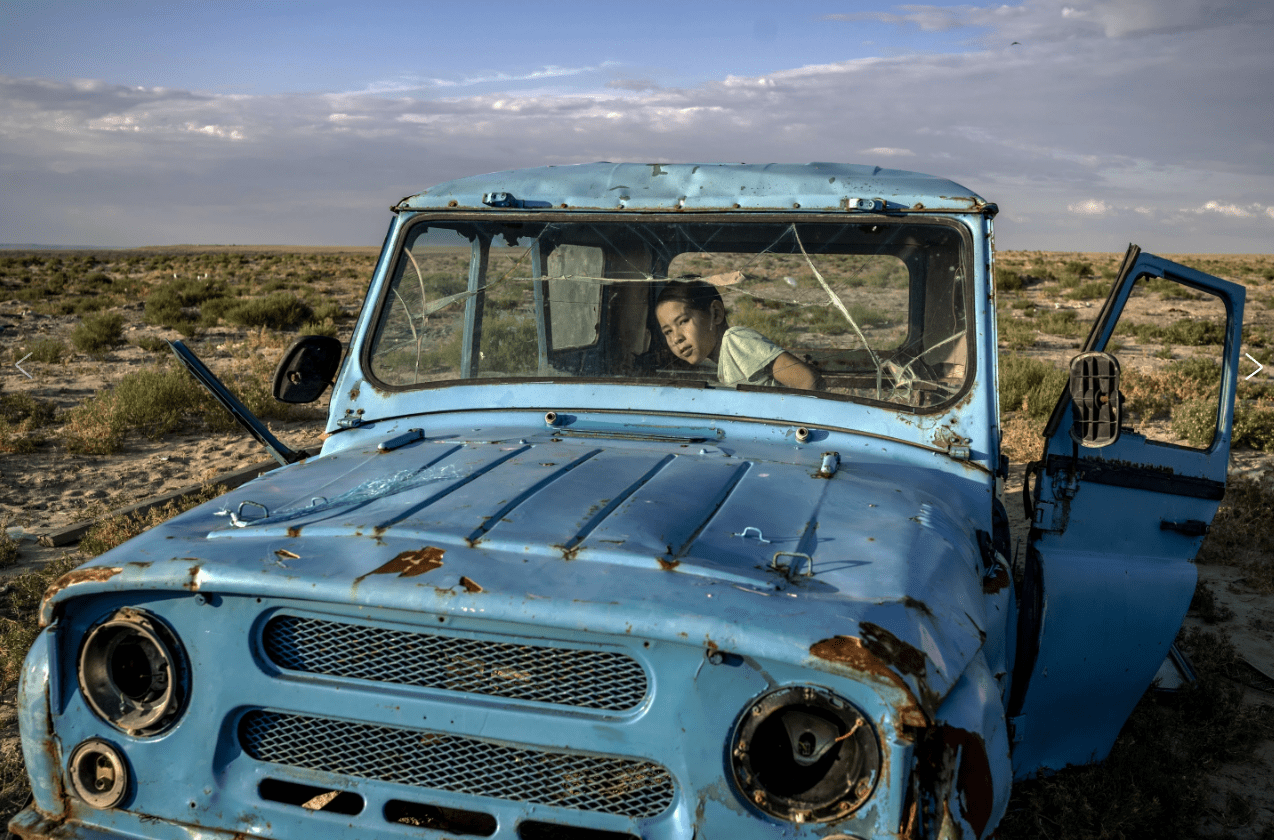 Ребенок играет в ржавой машине на берегу высохшего Аральского моря